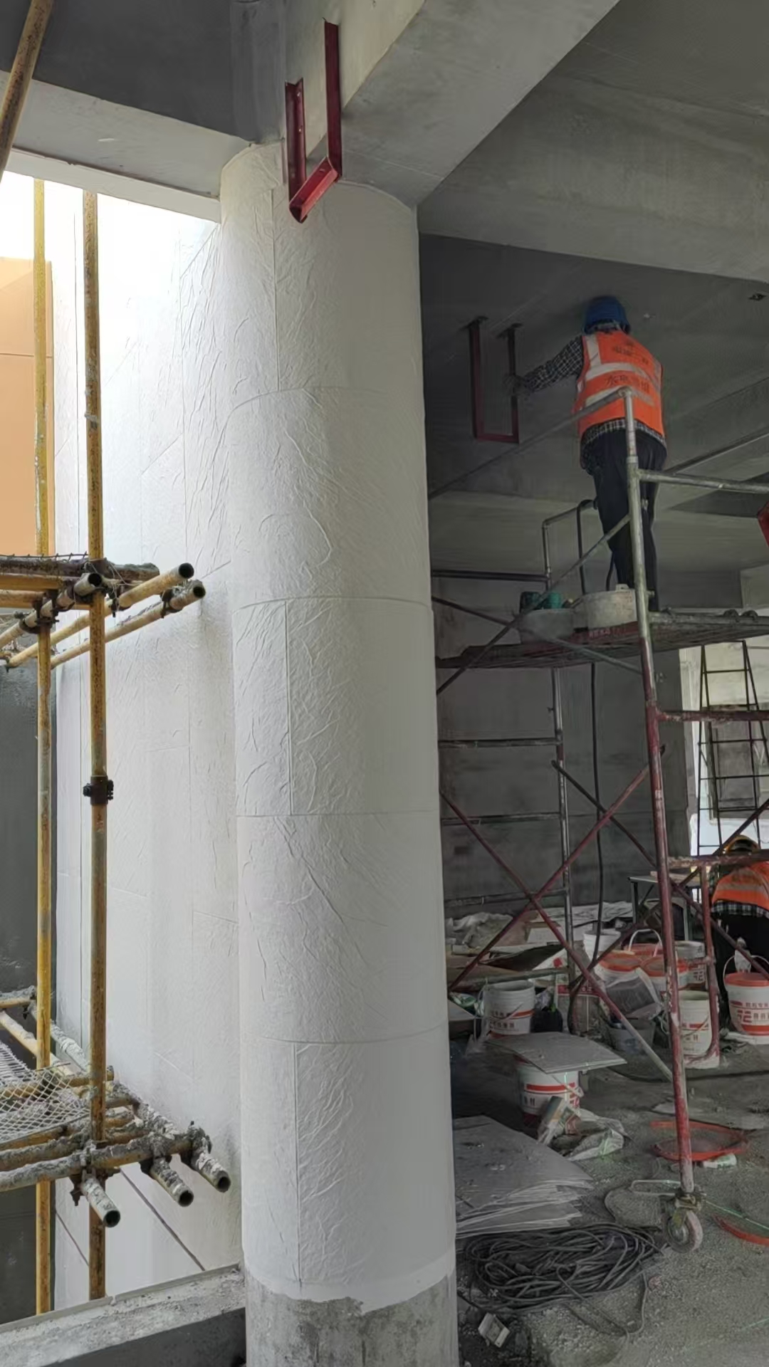 Installer wrapping a structural column with flexible stone cladding on a retail fitout site